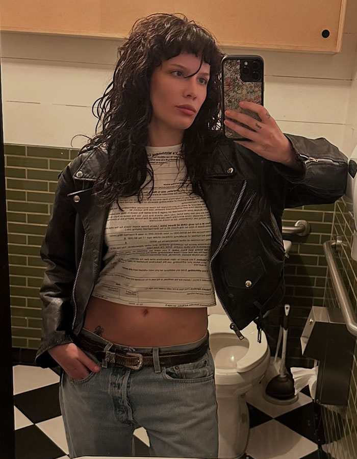 Person taking a mirror selfie in a leather jacket and cropped top, showing a visible tramp stamp tattoo trend. Person taking a mirror selfie in a leather jacket and cropped top, showing a visible tramp stamp tattoo trend.