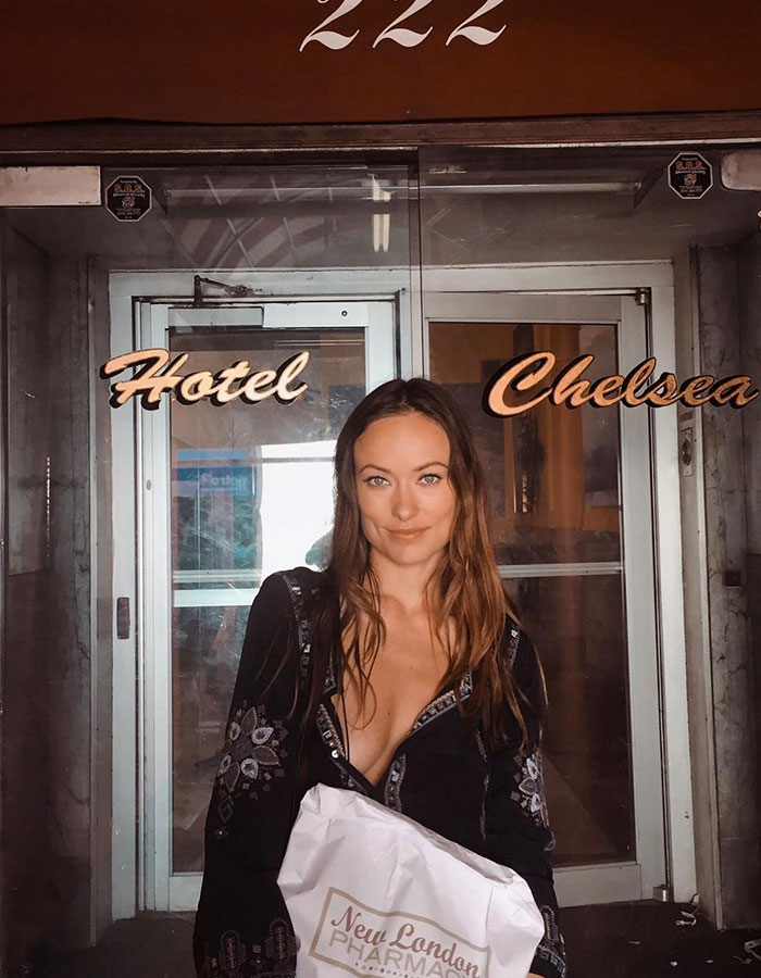 Young woman standing outside Hotel Chelsea holding a New London Pharmacy bag, representing tramp stamp tattoo trend revival. Young woman standing outside Hotel Chelsea holding a New London Pharmacy bag, representing tramp stamp tattoo trend revival.