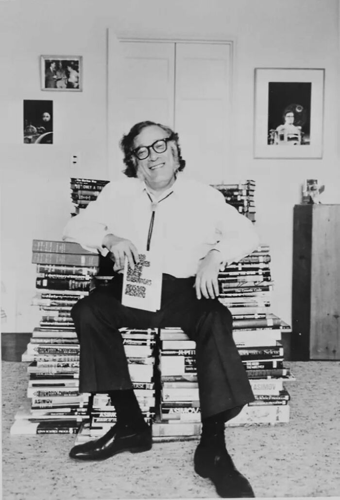 Man wearing glasses sitting on a chair made of stacked books, holding a book, symbolizing warnings ignored by the world.