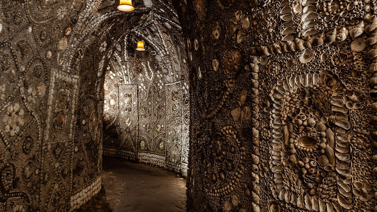 Underground grotto walls covered in millions of seashells forming intricate patterns under dim lights.