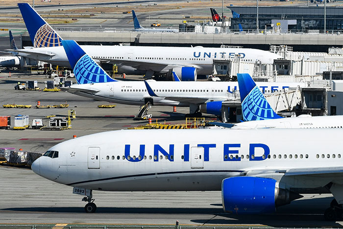 Multiple United Airlines planes parked at the airport tarmac near terminals on a sunny day Multiple United Airlines planes parked at the airport tarmac near terminals on a sunny day