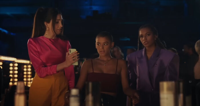 Three young women in stylish outfits at a dimly lit bar, representing characters hard to love in popular shows.