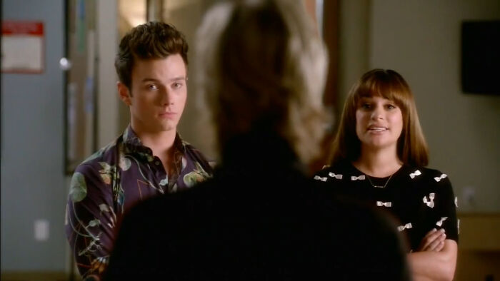 Two characters in a scene from a show, with one looking serious and the other smiling, depicting hard to love characters.