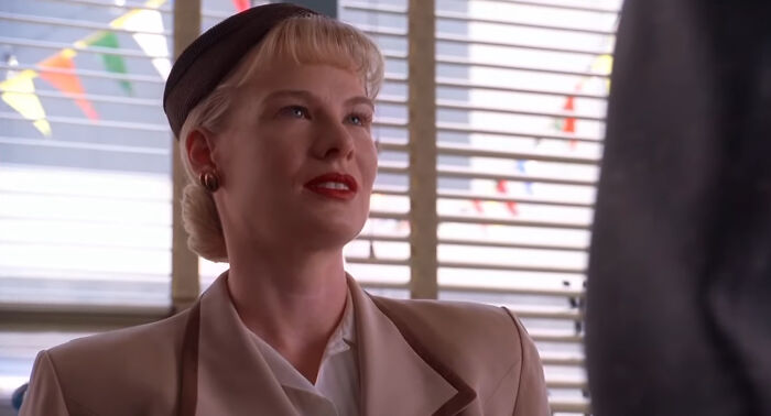 Woman with vintage hairstyle and attire sitting in a brightly lit room from shows with characters hard to love