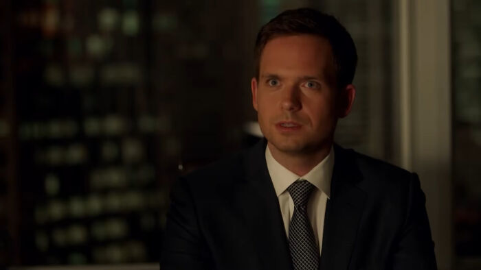 Man in suit and tie sitting indoors at night, representing shows with characters that are hard to love.