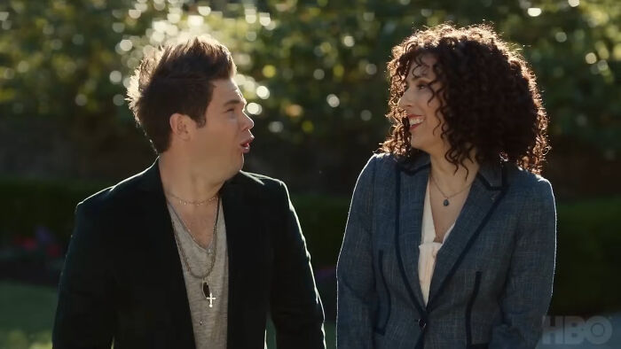 Two characters in an outdoor scene from a show with hard to love characters, engaged in conversation and smiling.