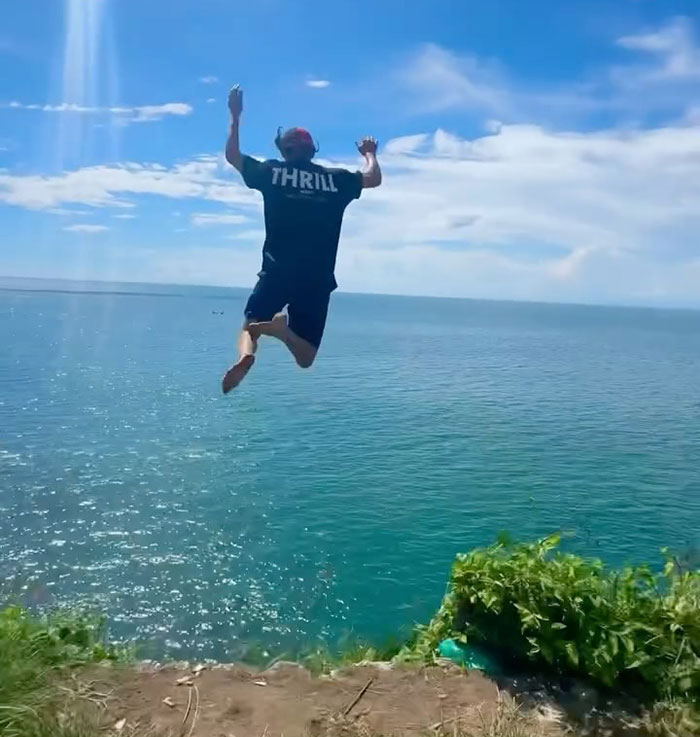 Young daredevil jumping off cliff into ocean attempting record-breaking dive on a sunny day with clear skies. Young daredevil jumping off cliff into ocean attempting record-breaking dive on a sunny day with clear skies.