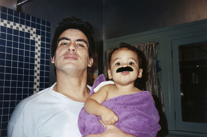Man holding toddler wrapped in purple towel with fake mustache, illustrating very rare boy names for stand-out babies.