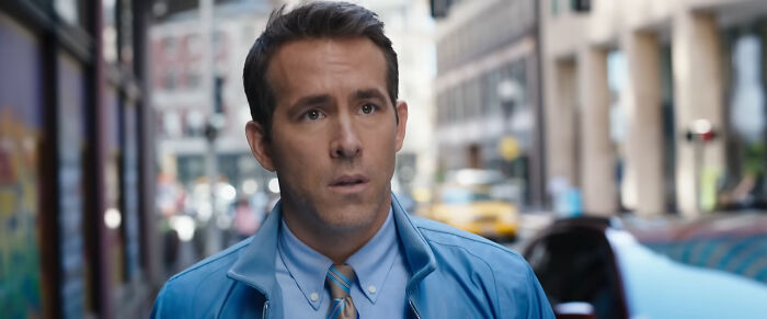Actor Ryan Reynolds in a blue jacket walking on a city street, representing celebrities many people love but can't stand.