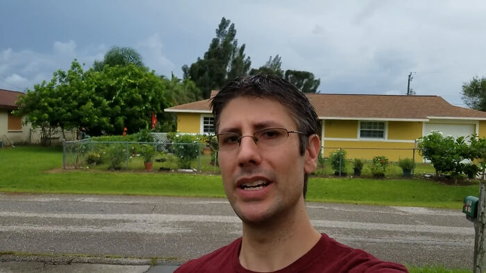 Man in glasses and red shirt speaking outdoors in a residential area, illustrating people share unsubscribed YouTubers concept.