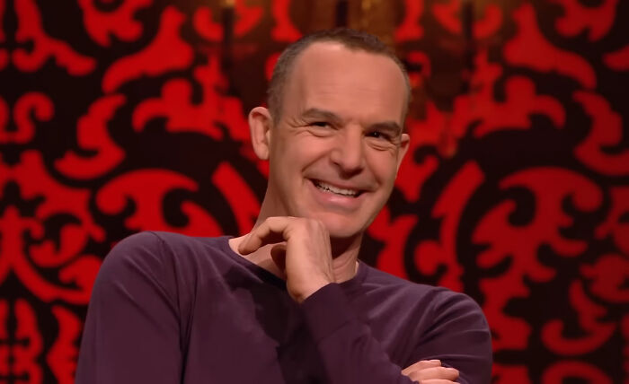 Man smiling during a TV show set with red and black patterned background, related to celebrities people can't stand topic