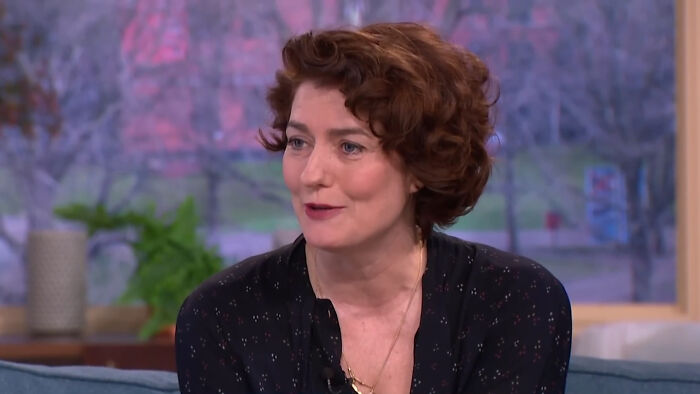 A woman with short curly hair wearing a dark patterned blouse, discussing celebrities many love but can't stand.