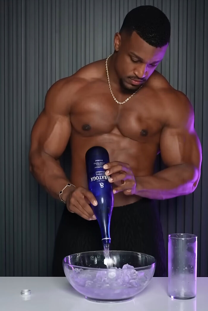 Muscular man pouring liquor into an ice-filled bowl, illustrating trends contributing to overconsumption concerns.