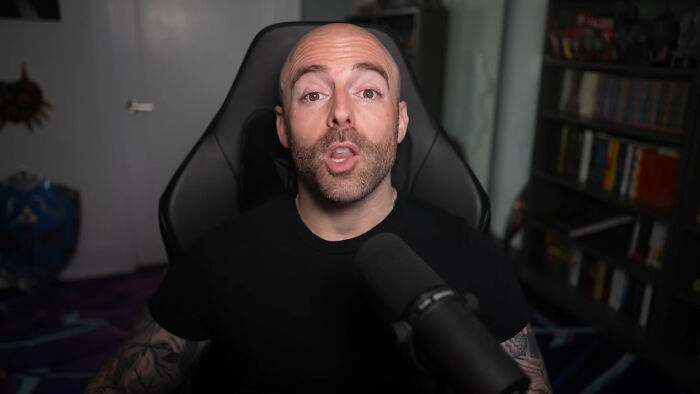 Man with a shaved head speaking into a microphone in a home office setting showing people share unsubscribed YouTubers trends.