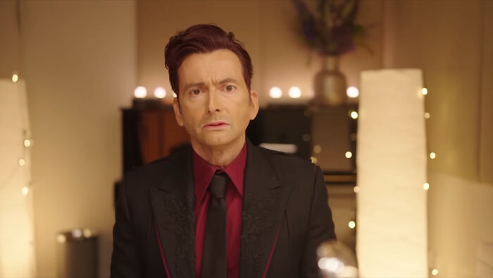 Man in a dark suit and red shirt speaking on camera in a softly lit room about celebrities many people can't stand.