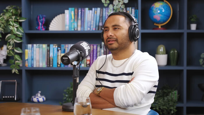 Man wearing headphones speaking on a podcast about celebrities many people love but honestly can't stand in a cozy studio.
