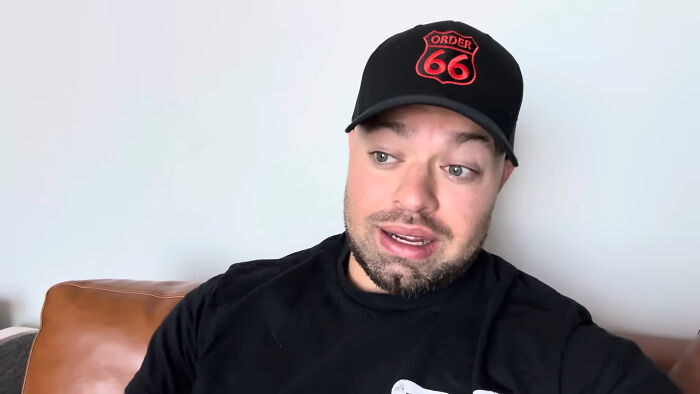 Man wearing a black cap and shirt sitting on a couch talking about people share unsubscribed YouTubers trends.