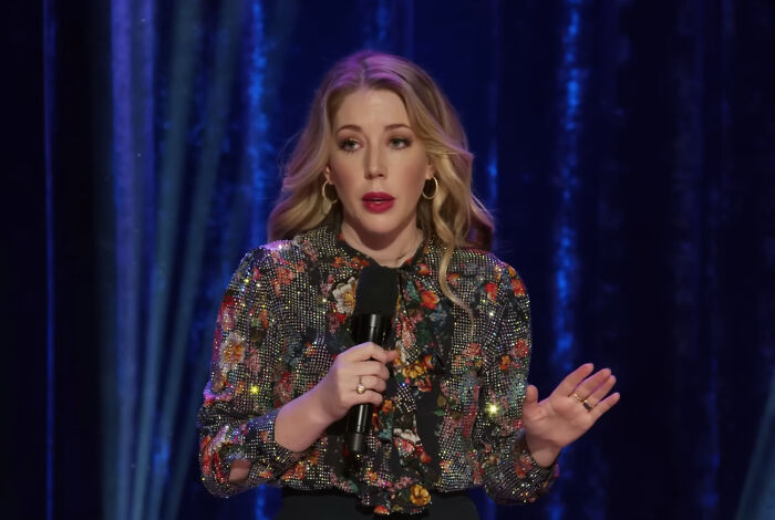 Female comedian on stage holding microphone, representing celebrities many people love but honestly can’t stand.