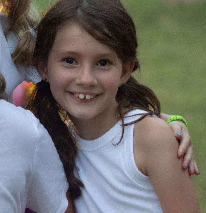 8-year-old girl smiling outdoors with braided hair, wearing a white tank top, representing horse walks behind her hearse. 8-year-old girl smiling outdoors with braided hair, wearing a white tank top, representing horse walks behind her hearse.