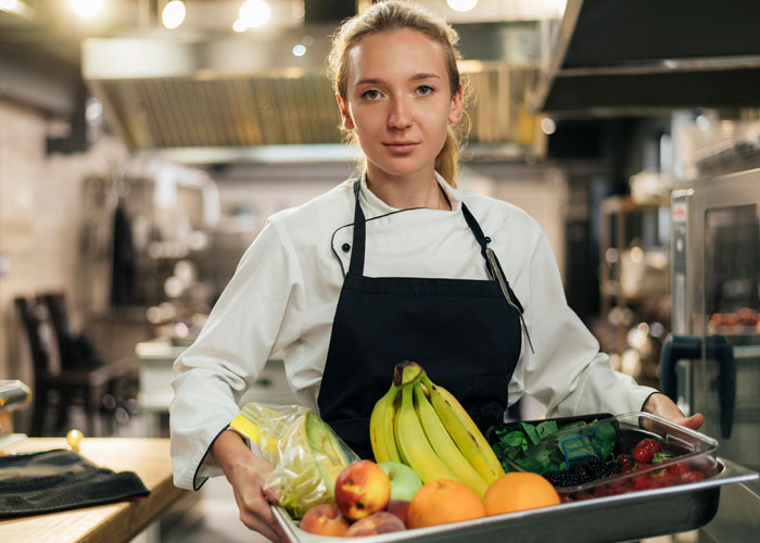 Female caterer holding a tray of fresh fruits in a professional kitchen, relating to bride's protests to change caterer. Female caterer holding a tray of fresh fruits in a professional kitchen, relating to bride's protests to change caterer.