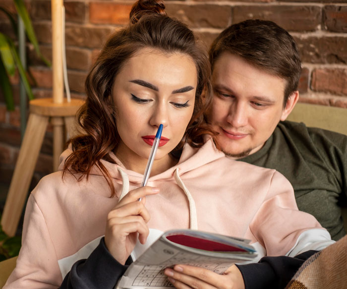 Bride thoughtfully holding pen while reading, with groom sitting close, illustrating bride's protests over wedding caterer choice. Bride thoughtfully holding pen while reading, with groom sitting close, illustrating bride's protests over wedding caterer choice.