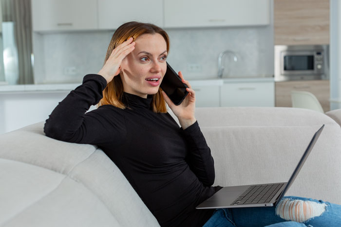 Woman talking on phone with laptop on lap, depicting conflict and friendship in a casual home setting.