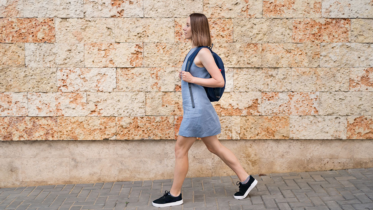Young woman walking outdoors with a backpack, illustrating weird habits that might improve mental and physical health benefits.