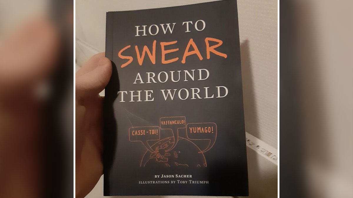 Hand holding a book titled How to Swear Around the World, a weird book perfect for adding personality to your bookshelf.