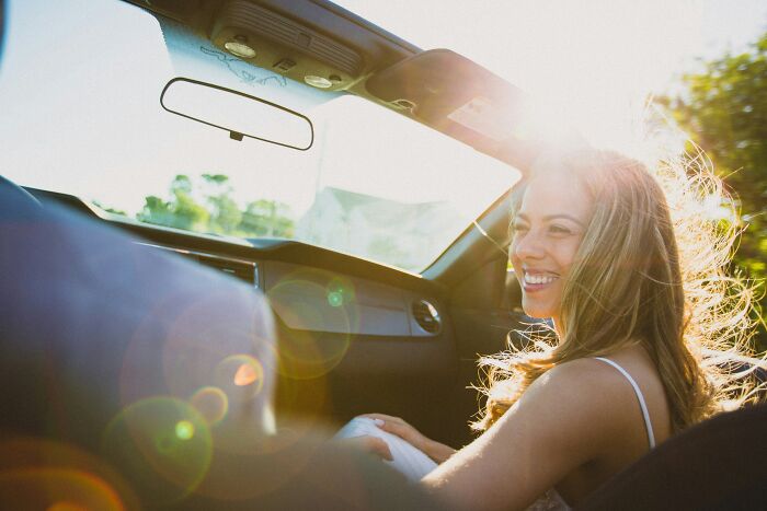 Smiling woman passenger enjoying a sunny car ride while truckers share craziest things seen on the road.