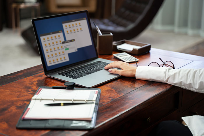 Worker at desk using laptop with documents and glasses nearby, appearing annoyed while avoiding birthday cake celebration. Worker at desk using laptop with documents and glasses nearby, appearing annoyed while avoiding birthday cake celebration.