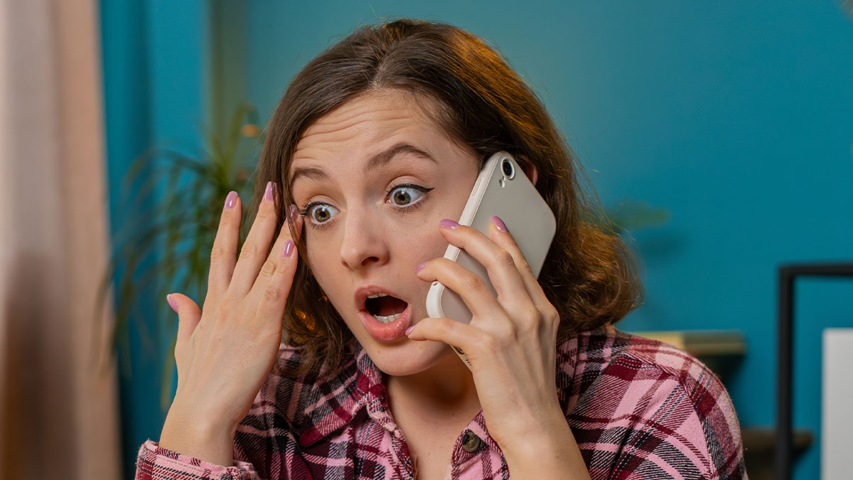 Woman in a pink plaid shirt looks shocked while talking on phone, reflecting co-parent misunderstanding and CPS involvement.