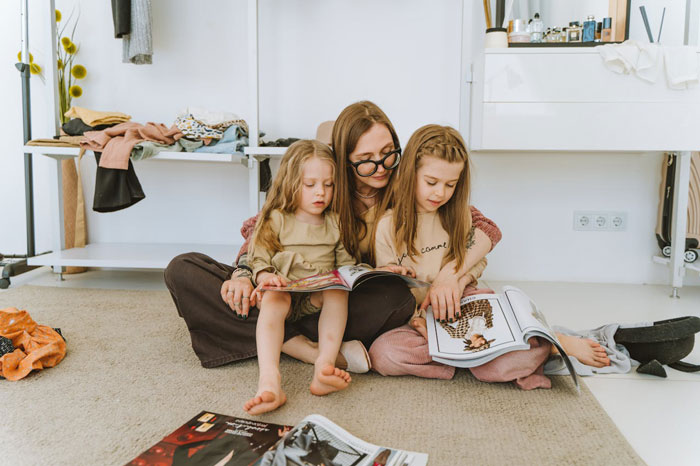 Woman sitting on floor reading magazines with two young girls, reflecting on cutting off friend in abusive marriage. Woman sitting on floor reading magazines with two young girls, reflecting on cutting off friend in abusive marriage.