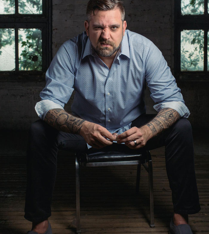 Man with tattoos sitting on a chair in a dim room, showing emotions related to cutting off a friend in abusive marriage. Man with tattoos sitting on a chair in a dim room, showing emotions related to cutting off a friend in abusive marriage.