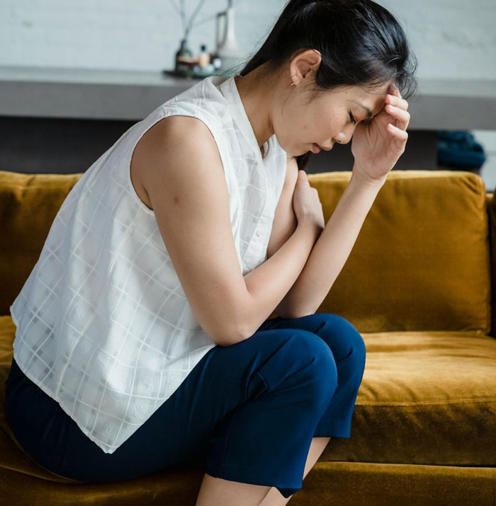 Woman sitting on a couch looking distressed, reflecting feelings related to cutting off a friend in an abusive marriage Woman sitting on a couch looking distressed, reflecting feelings related to cutting off a friend in an abusive marriage