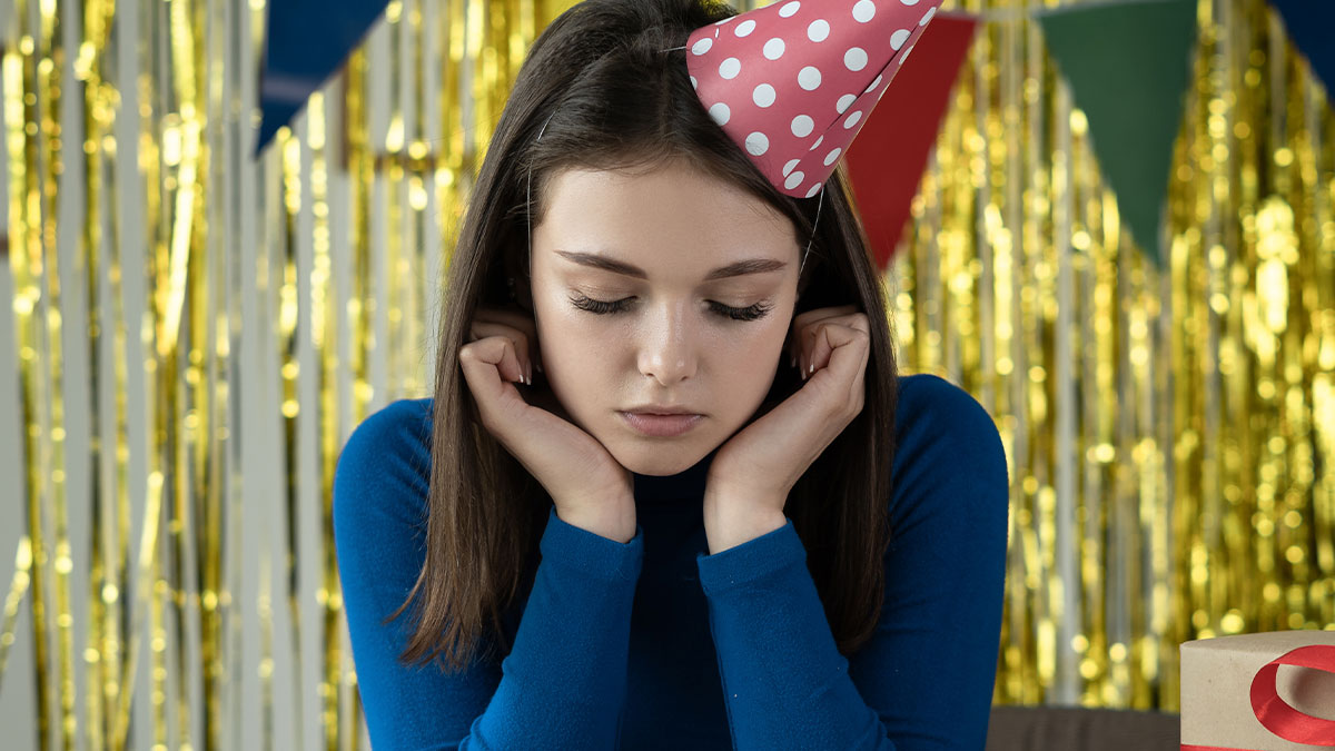Sad woman in a party hat looking down, illustrating jerk boyfriend behavior and dream gift disappointment scene.