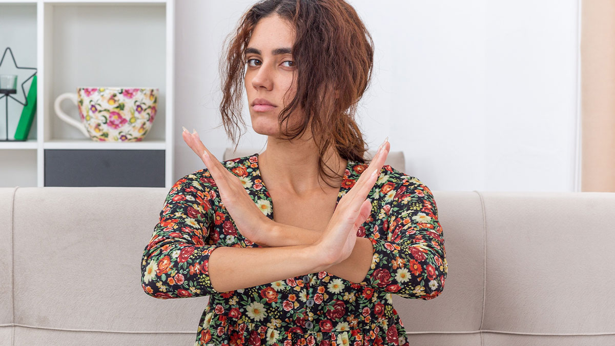 Woman wearing floral dress sitting on couch with arms crossed in refusal gesture, showing organ donor refusal concept.