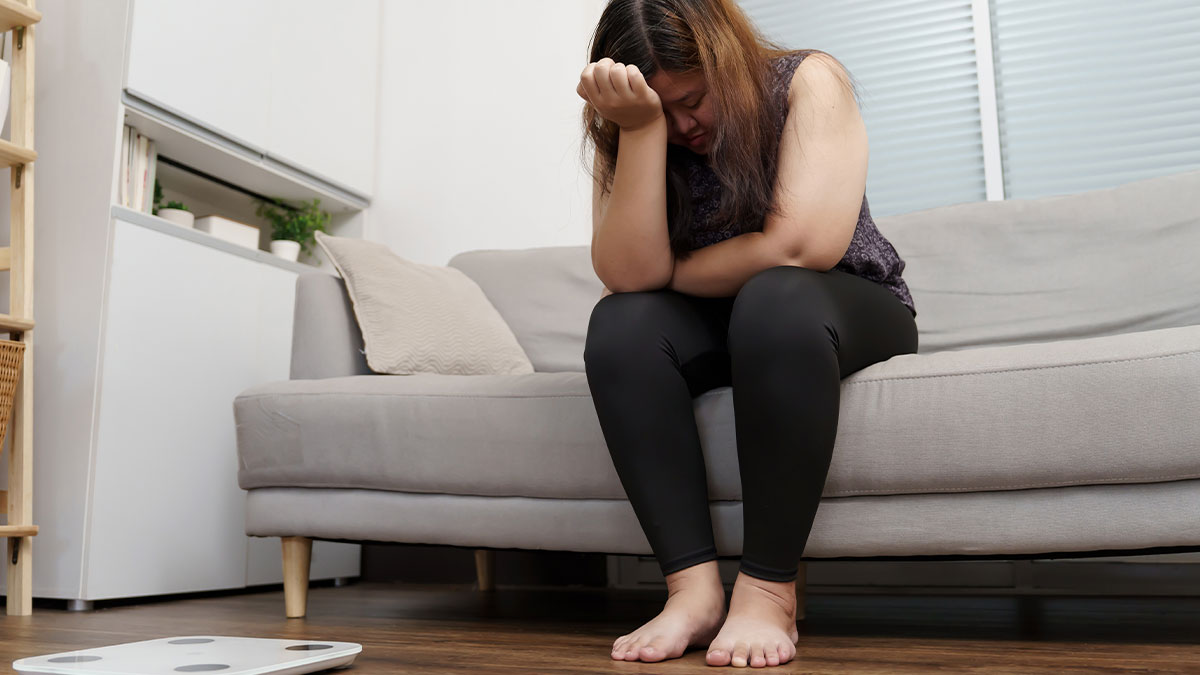 Woman sitting on couch looking shocked and upset after overhearing boyfriendu2019s parents talking about her at home.