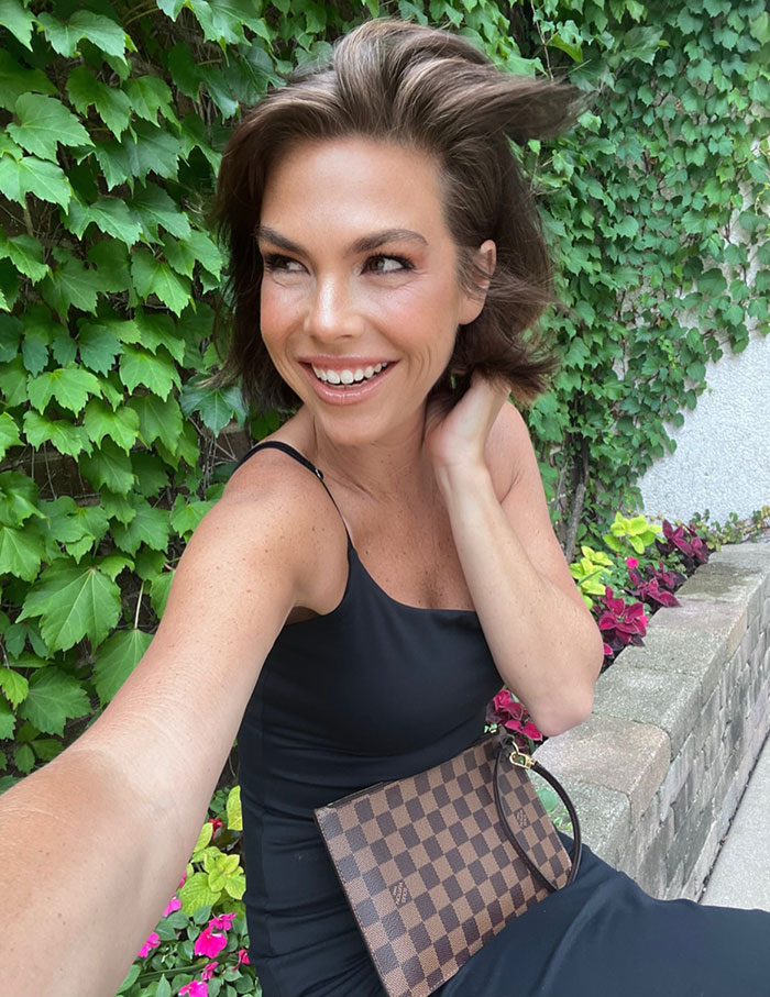 Intersex woman with XY chromosome smiling outdoors by greenery, wearing black dress and holding checkered purse. Intersex woman with XY chromosome smiling outdoors by greenery, wearing black dress and holding checkered purse.