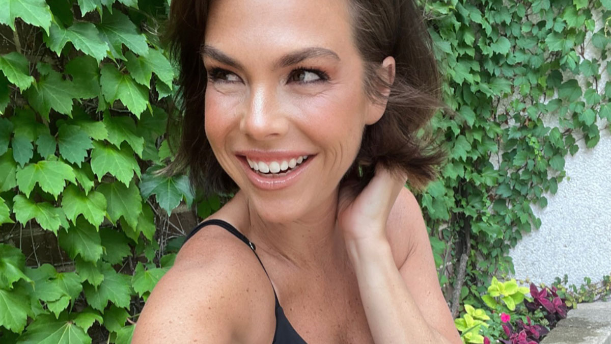 Intersex woman with XY chromosome smiling outdoors by green leafy plants, sharing her unique body differences.