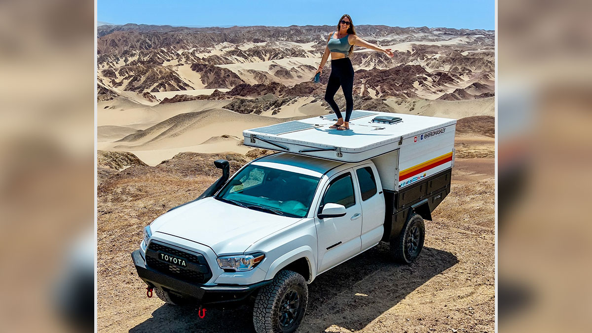 Woman standing on a white camper truck in a desert landscape, embracing van life and travel adventure.