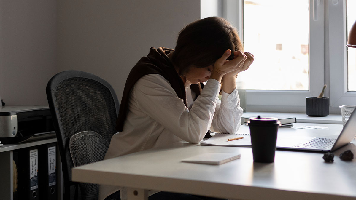 Woman stressed at a desk with laptop and coffee, contemplating work and making a decision to reapply for position.
