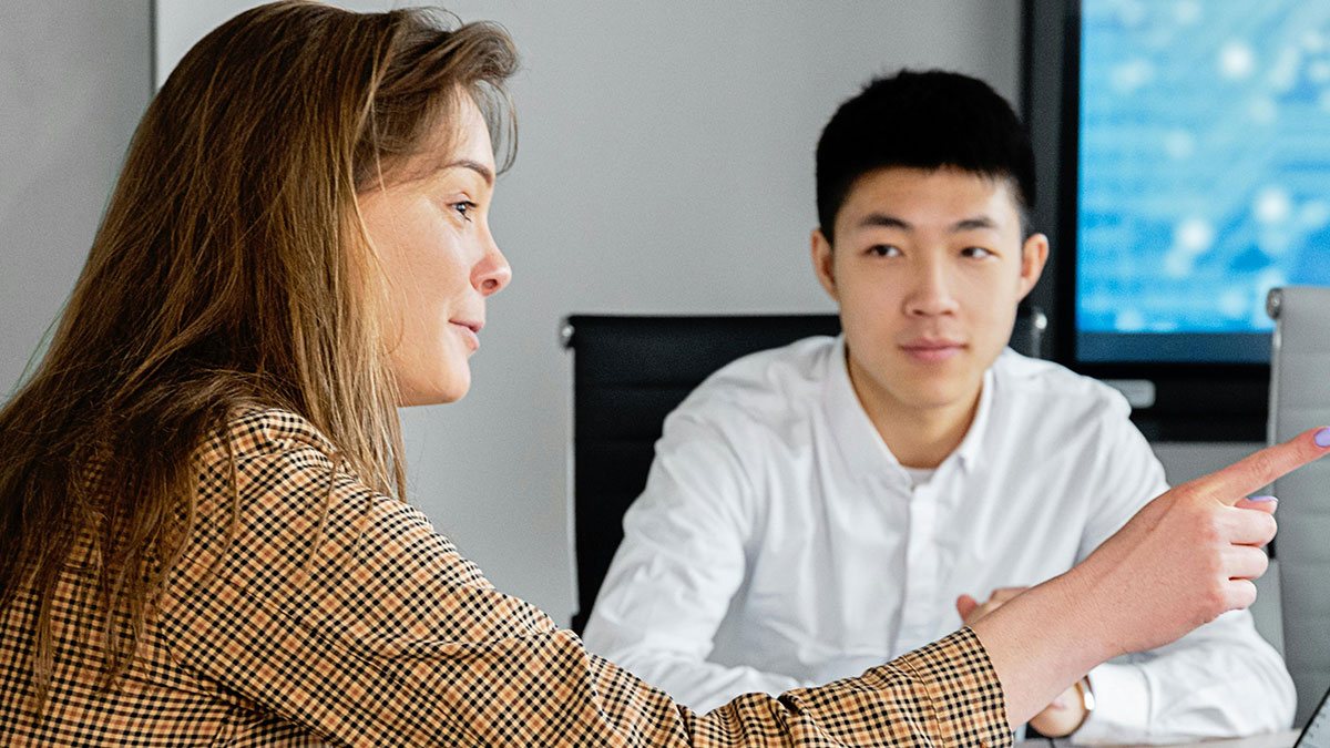 Two coworkers in a meeting, one pointing ahead as a sign of micromanagement in the workplace setting.