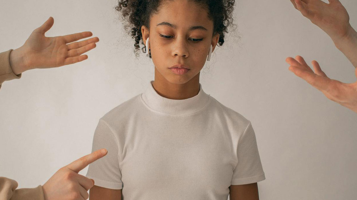 Young woman with earbuds looks down while multiple hands point and gesture around her, showing toxic friendship behavior.