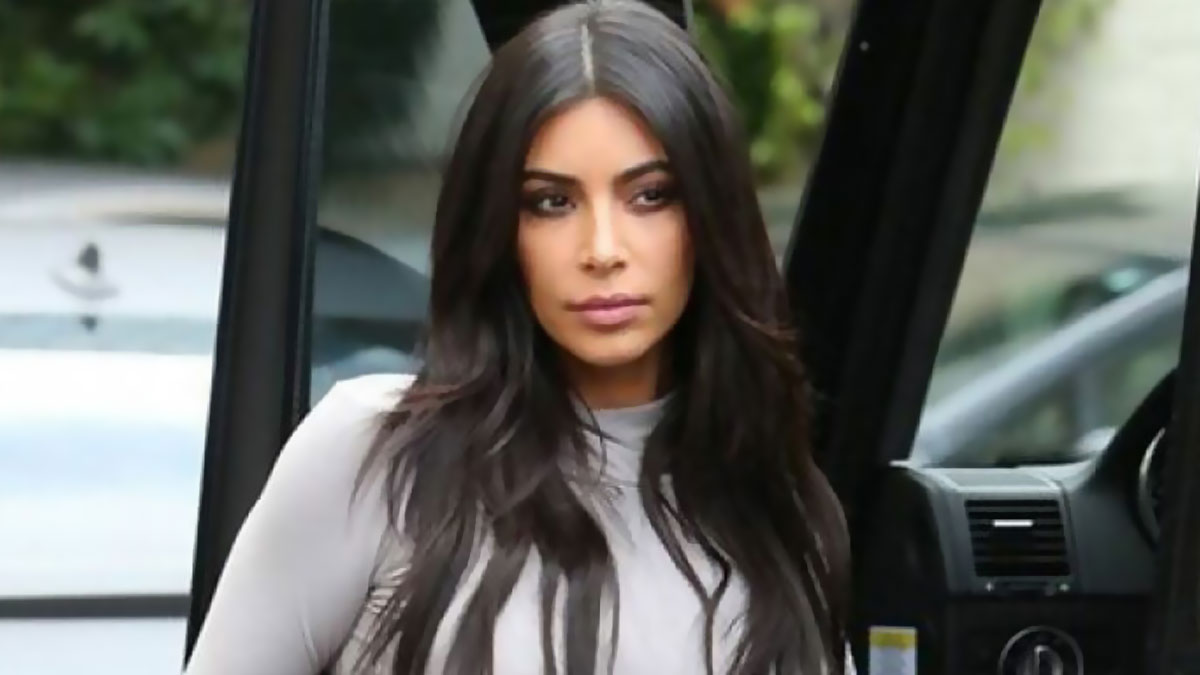 Kim Kardashian from KarJenner clan stepping out of a vehicle, wearing a light gray top with long dark hair outdoors.