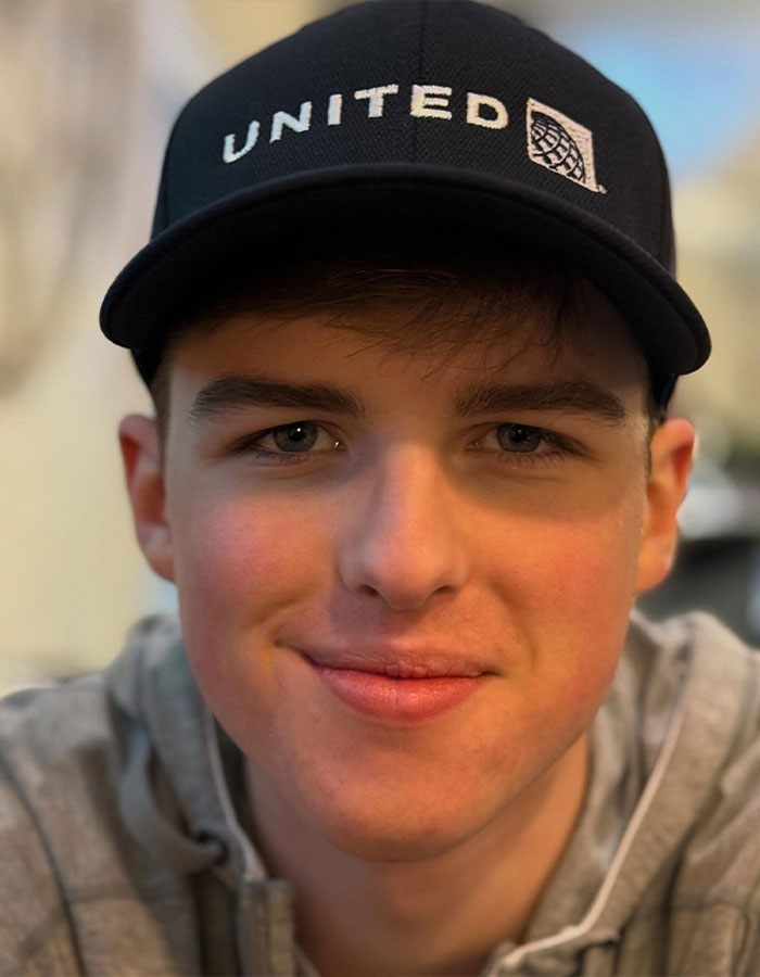 Teenage Young Sheldon child star wearing a black United cap and gray hoodie, smiling in a close-up portrait. Teenage Young Sheldon child star wearing a black United cap and gray hoodie, smiling in a close-up portrait.