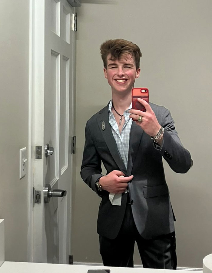 Young Sheldon child star at 17 wearing a suit, smiling and taking a mirror selfie in a bathroom. Young Sheldon child star at 17 wearing a suit, smiling and taking a mirror selfie in a bathroom.
