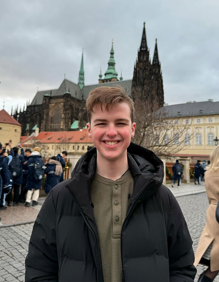 Young Sheldon child star at 17, smiling outdoors in a black jacket with historic buildings in the background. Young Sheldon child star at 17, smiling outdoors in a black jacket with historic buildings in the background.