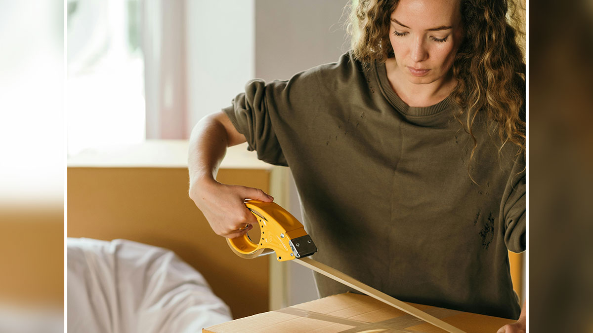 Young woman packing and taping boxes as she prepares to move out feeling burdened by sibling responsibilities.