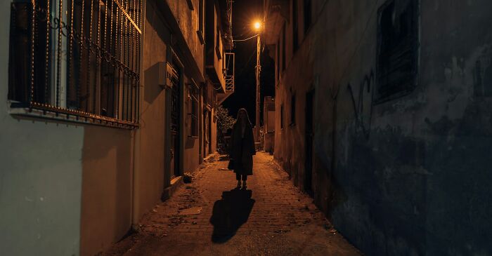 Person standing alone in a narrow dimly lit alley at night, highlighting challenges in communicating calmly skills.