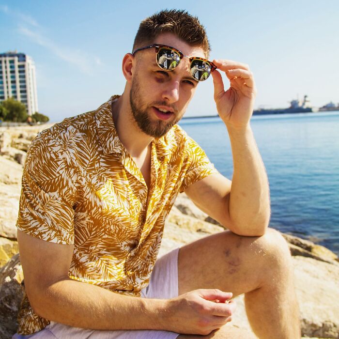 Young man adjusting sunglasses while sitting near water, sparking influencer outrage for filming indigenous tribe viral stunt. Young man adjusting sunglasses while sitting near water, sparking influencer outrage for filming indigenous tribe viral stunt.